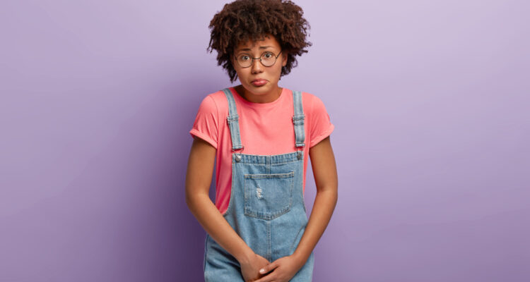 a young woman with brown hair dressed in a bright pink shirt and blue denim dungarees.