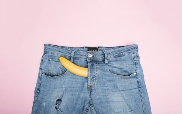 blue jean trousers against a pink background with a yellow peeking out through the fly