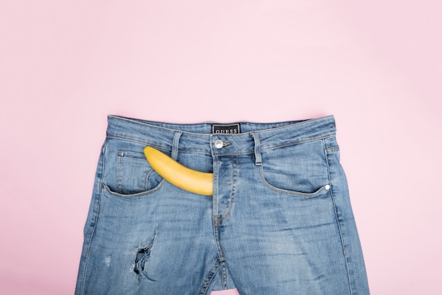 blue jean trousers against a pink background with a yellow peeking out through the fly